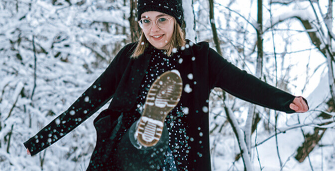 Frau mit Mütze kickt Schnee