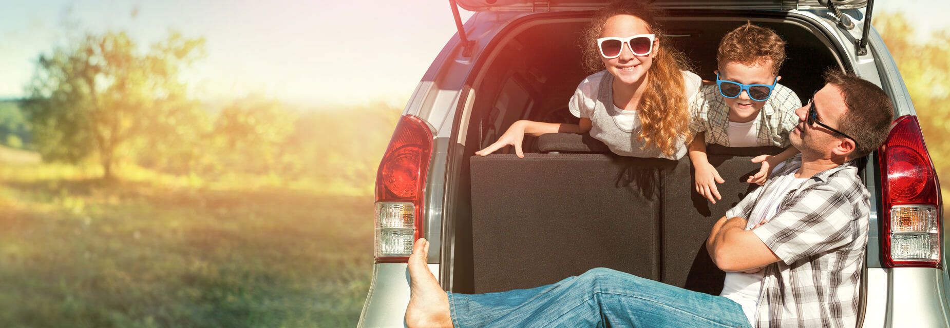 Vater und Kinder sitzen fröhlich im offenen Kofferraum ihres Autos