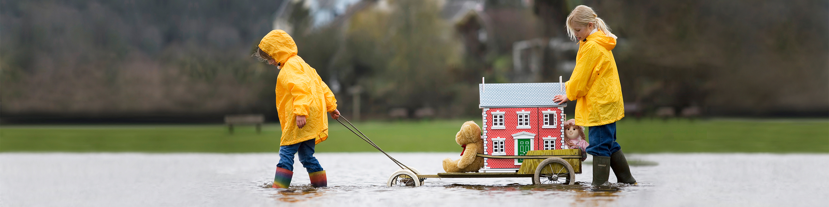 Kinder ziehen Spielzeughaus auf Wagen durchs Hochwasser - ihr Haus ist dank der Wohngebäudeversicherung der SV gut abgesichert