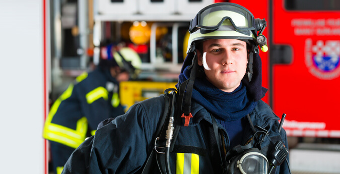 Feuerwehrförderung - Feuerwehrmann in voller Montur vor Feuerwehrwagen