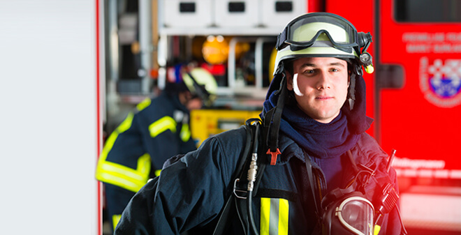 Feuerwehrförderung - Feuerwehrmann in voller Montur vor Feuerwehrwagen