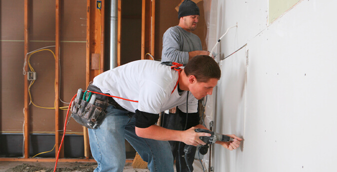 Bauhelfer-Unfallversicherung - Bauarbeiter streichen eine Wand