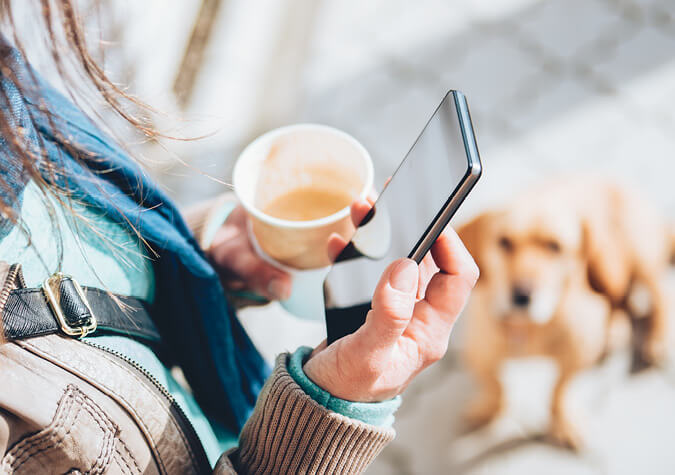 Frau schaut auf ihr Smartphone und Hund im Hintergrund