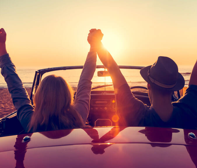 Zusatzfahrerversicherung - Paar im Auto bei Sonnenuntergang