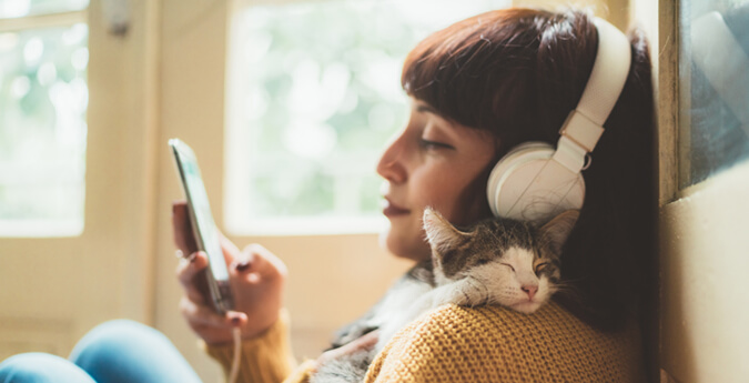 Corona FAQ - Frau mit Kopfhörer und Katze am Handy